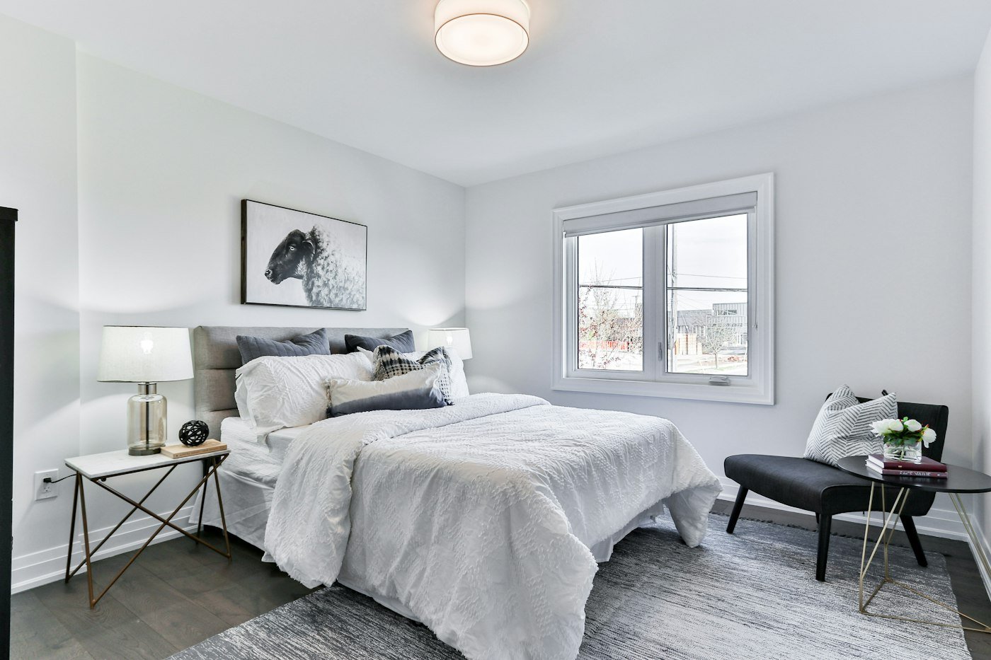 A white bedroom with a grey headboard, a picture of a sheep, and a window to the right